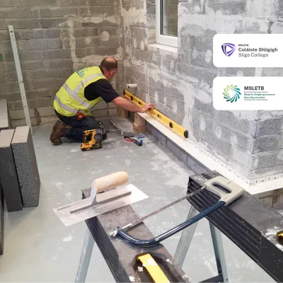 Construction worker in yellow vest using a spirit level on a floor during bricklaying work indoors.