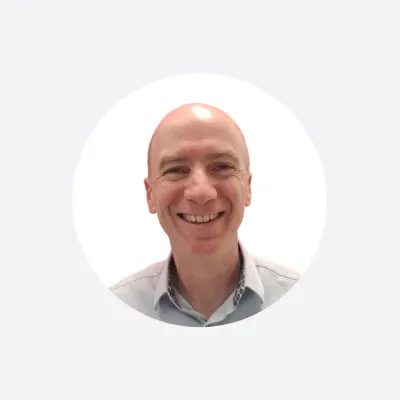 Smiling bald man in a light blue shirt, circular cropped headshot photo.