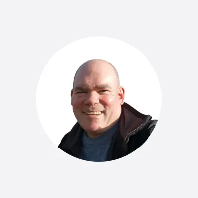 Smiling bald man in a dark jacket, photographed outdoors in natural light.
