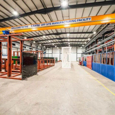 Large industrial warehouse with orange overhead crane, metal frames, and blue equipment along the walls.