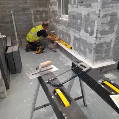 Construction worker in high-vis vest using a spirit level on a concrete block wall at a building site.