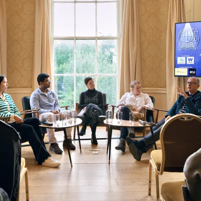 Six people seated in a semicircle during a panel discussion, with a "Postdoc Spotlight" screen behind them.