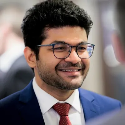 Young man with glasses and a red tie smiling warmly in a professional setting.