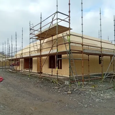 Wooden-framed house under construction with scaffolding on a cloudy day.