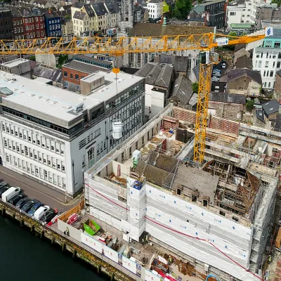 Aerial view of an active urban construction site with yellow cranes beside a waterfront.