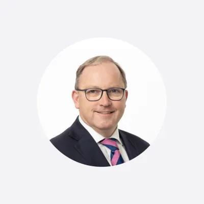 Professional headshot of a middle-aged man in a dark suit and striped tie, wearing glasses.