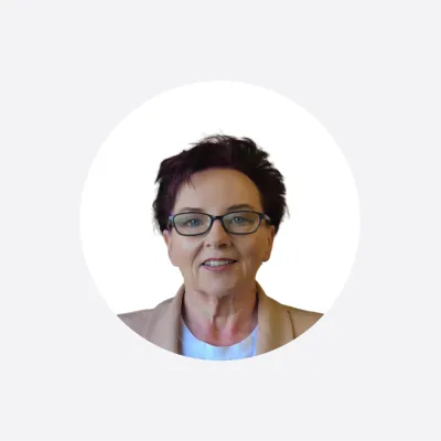 Headshot of an older woman with short dark hair and glasses, wearing a tan blazer.