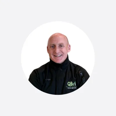 Smiling man in a black QBri uniform, circular cropped portrait photo.