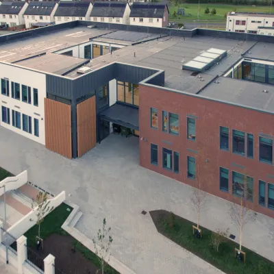 Aerial view of a modern school complex with brick and gray buildings, surrounded by pathways and grass.
