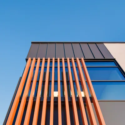 Modern building corner with warm wooden vertical slats and large windows against a clear blue sky.