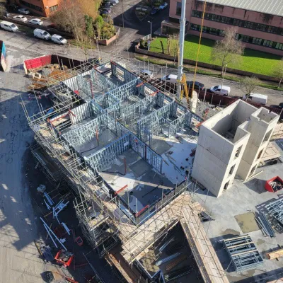 Aerial view of a building under construction with scaffolding and steel framework on a cloudy day.
