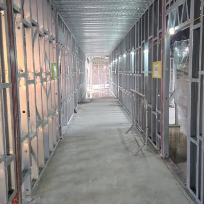 Long narrow corridor under construction with metal framing and drywall panels on both sides.