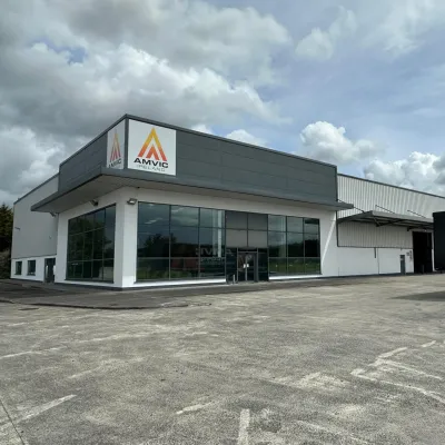 Modern commercial building with yellow triangle logo, large windows, and a truck parked outside.