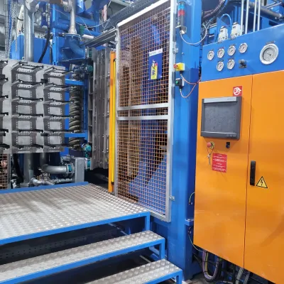 Industrial manufacturing machine with blue and orange metal framework, control panel, and safety cage.