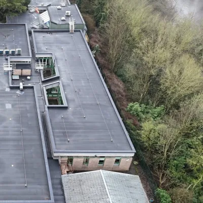 Aerial view of a flat-roofed industrial building beside dense green trees on a misty day.