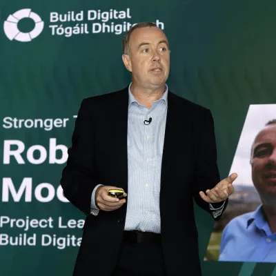 Man presenting at a Build Digital event, standing at a podium with a profile slide behind him.