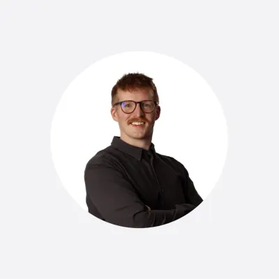 Smiling man with glasses wearing a dark shirt, arms crossed, in a circular profile photo.