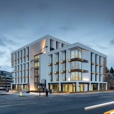 Modern multi-story office building with illuminated facade at dusk, light trails from passing traffic.