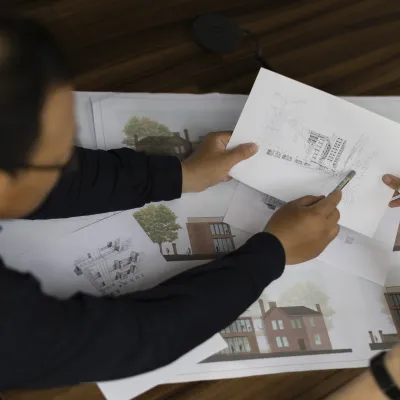 Two people reviewing architectural drawings and sketches spread on a table.