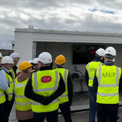 Group of workers in high-visibility jackets and hard hats gathered outside a construction site building.