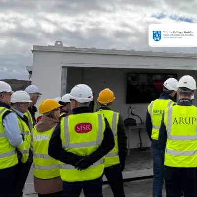 Group of construction workers in hi-vis vests and hard hats inspecting an outdoor facility.