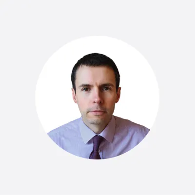 Professional headshot of a man in a light blue shirt and purple tie, circular crop.