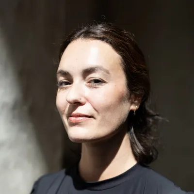 Woman with dark hair pulled back, wearing a black top, smiling softly in natural light.