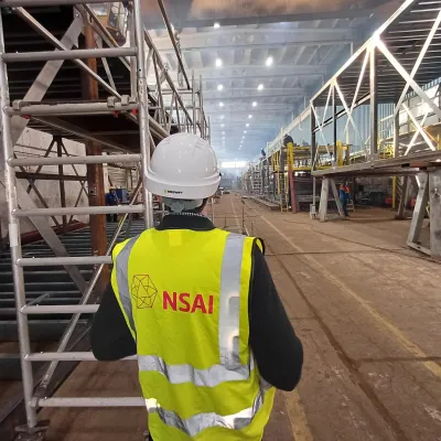 Worker in a yellow high-visibility vest and hard hat inspecting a large industrial warehouse interior.