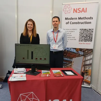 Two people standing at an NSAI exhibition booth with a red tablecloth and informational display.