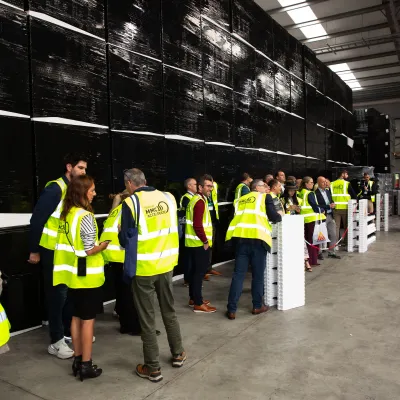 Group of visitors in yellow safety vests touring an industrial facility with large black equipment.