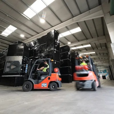 Two orange forklifts operating inside a large industrial warehouse with high ceilings.