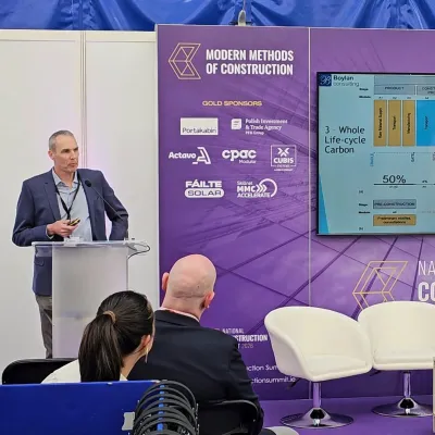 Man presenting at a construction industry conference with a colorful data chart displayed on screen.