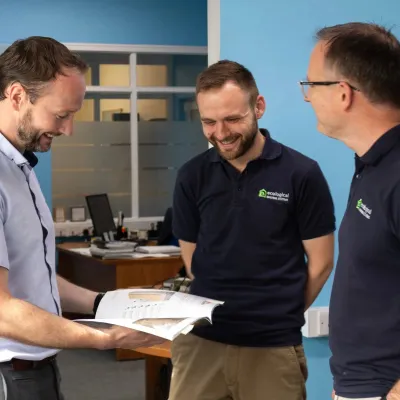 Three men smiling and reviewing documents together in an office setting.