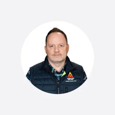 Man in a navy puffer vest with a company logo, smiling against a white background.