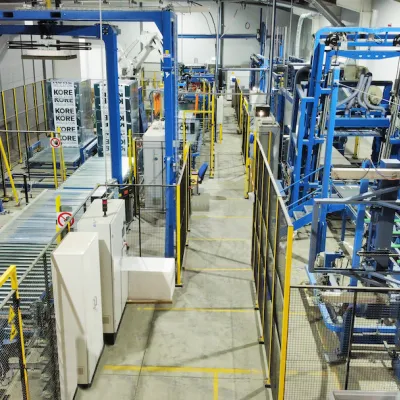 Industrial manufacturing facility with blue metal frames, conveyor systems, and white panels on the floor.