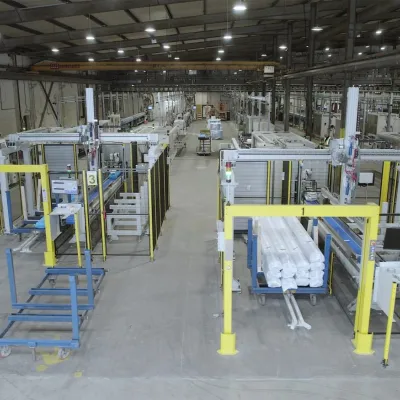 Large industrial warehouse with yellow safety railings, machinery, and conveyor systems on a white floor.
