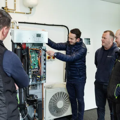 A trainer demonstrates a heat pump system to a group of attentive workers in a workshop setting.