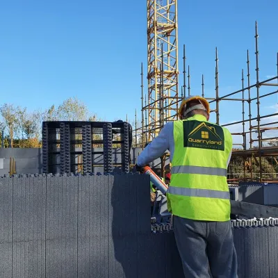 Construction worker in a hi-vis vest inspecting a building site with scaffolding and a crane.