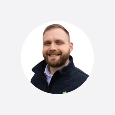 Smiling bearded man in a dark jacket, circular cropped professional headshot photo.