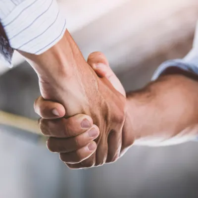 Two people shaking hands, one wearing an orange safety vest, symbolizing a business agreement.