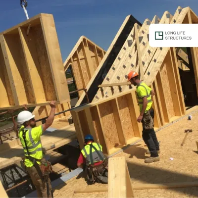 Construction workers in high-visibility vests assembling wooden wall frames for a new building.