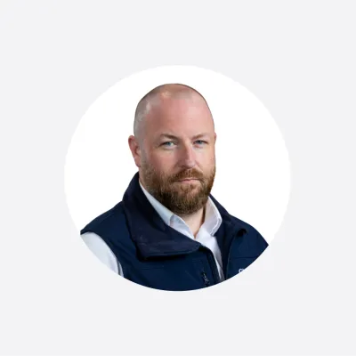 Professional headshot of a bearded man in a navy vest and white shirt, circular crop.