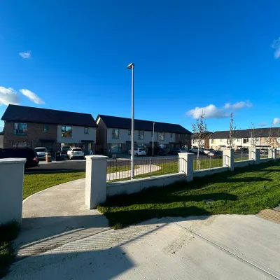 Suburban street with white fence, houses, and a tall lamp post under a bright blue sky.