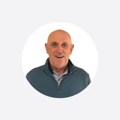 Smiling bald man in a blue zip-up jacket, circular portrait photo.