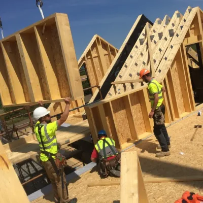 Construction workers in high-visibility vests assembling wooden wall frames for a new building.