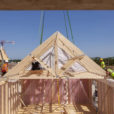 Wooden roof truss being lifted by crane onto a timber-frame building under construction.